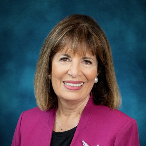 Jackie Speier smiling in a professional headshot, wearing a magenta blazer with a bird-shaped brooch