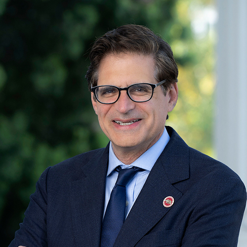 Josh Becker smiling in a professional headshot, wearing glasses and a navy suit